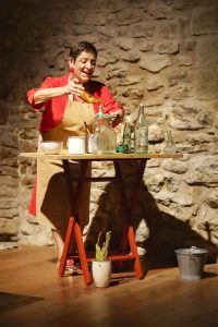 Mujer realizando experimento científico con líquidos en escenario teatral.