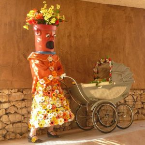 Personaje disfrazado de flor con carrito en evento cultural.